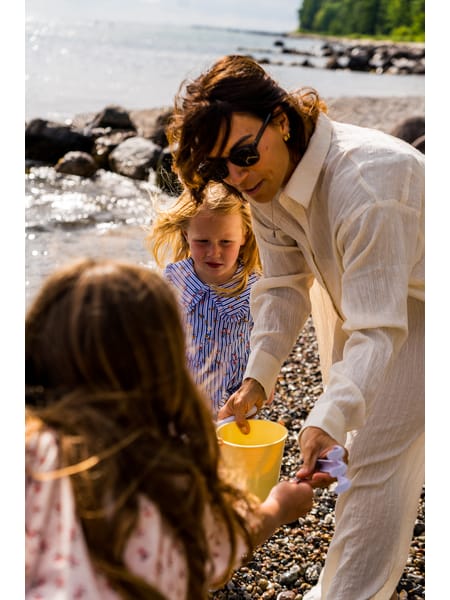 Gul spand og grøn skovl ligger på sandet ved vandkanten med små skaller omkring